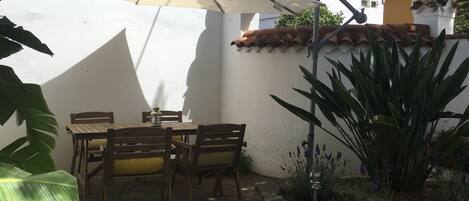 Une terrasse avec une table et des chaises, entourée de plantes et d’un mur en pierre.