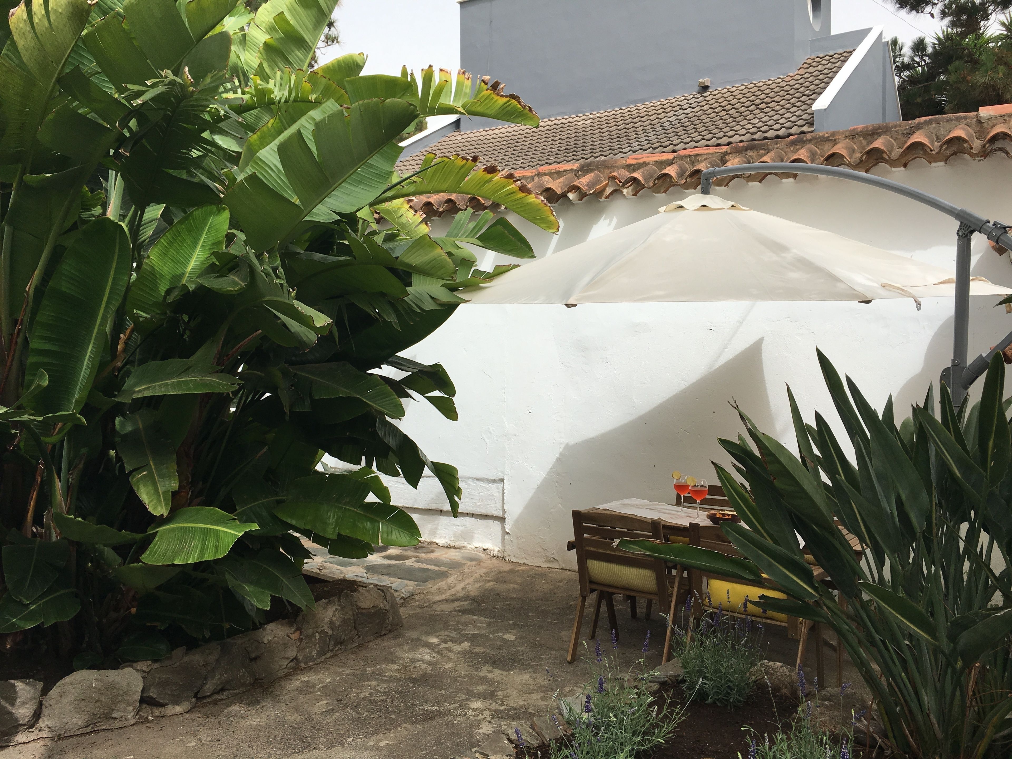 Een terras met een stenen muur, een witte parasol en een tafel met stoelen.