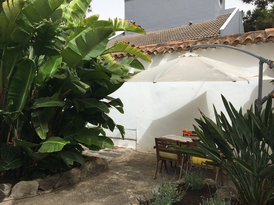 Zona de pati amb mur de pedra, una paraigua blanca i taula amb caires.