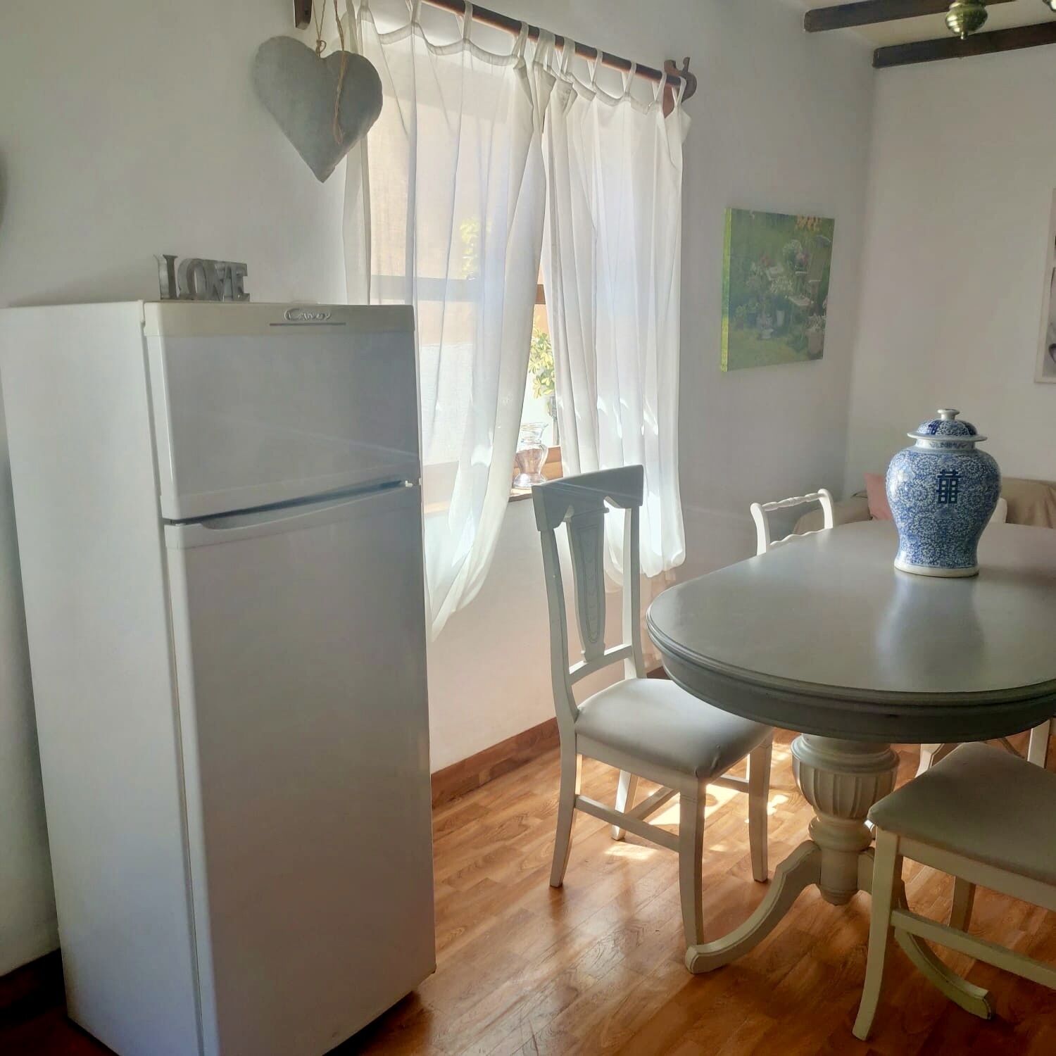 Una cocina compacta con un refrigerador blanco, una mesa redonda con sillas y un florero azul sobre la mesa.