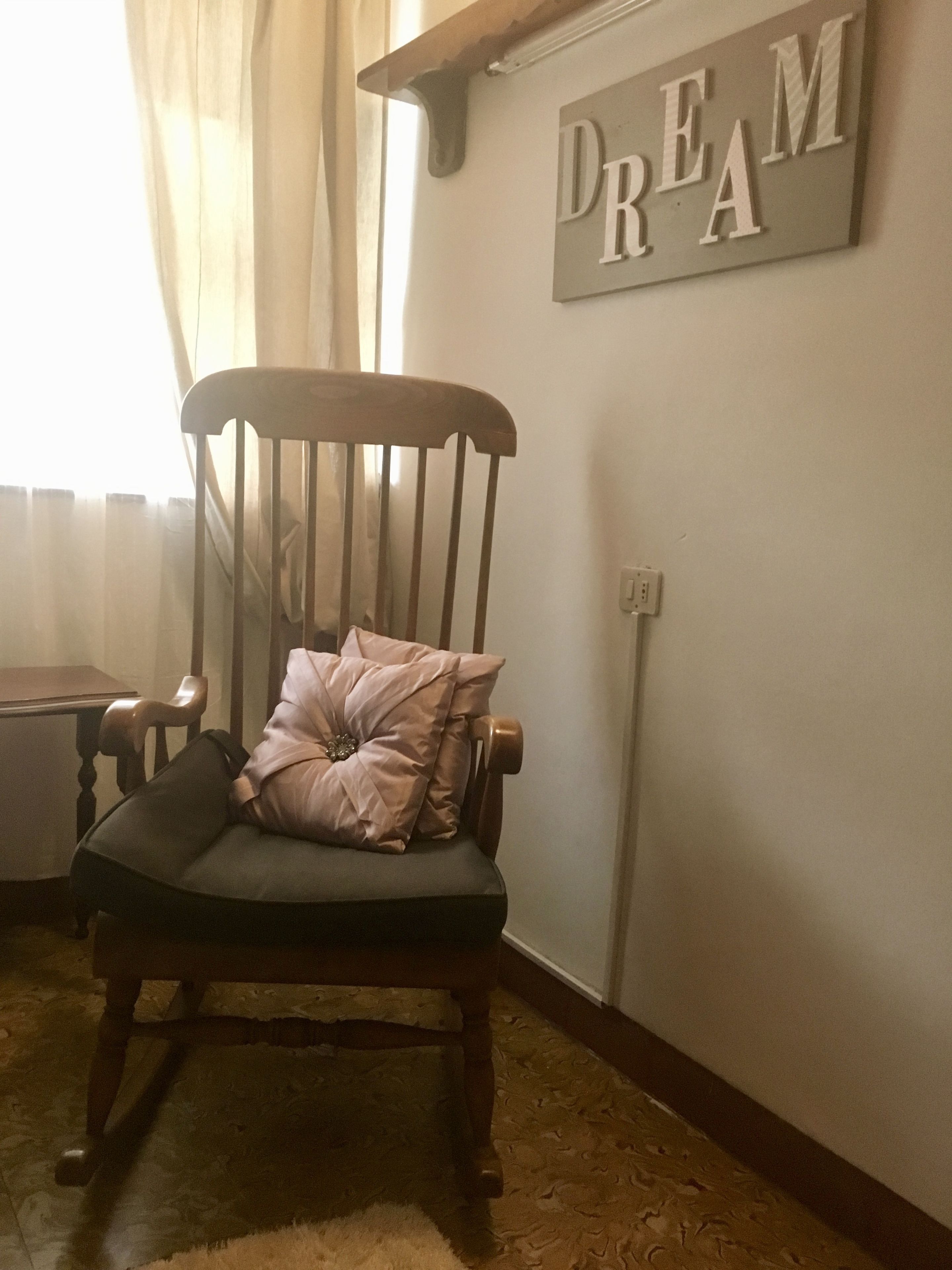 Una silla de madera con un cojín y una almohada decorativa, ubicada en una habitación con un letrero en la pared que dice "DREAM".