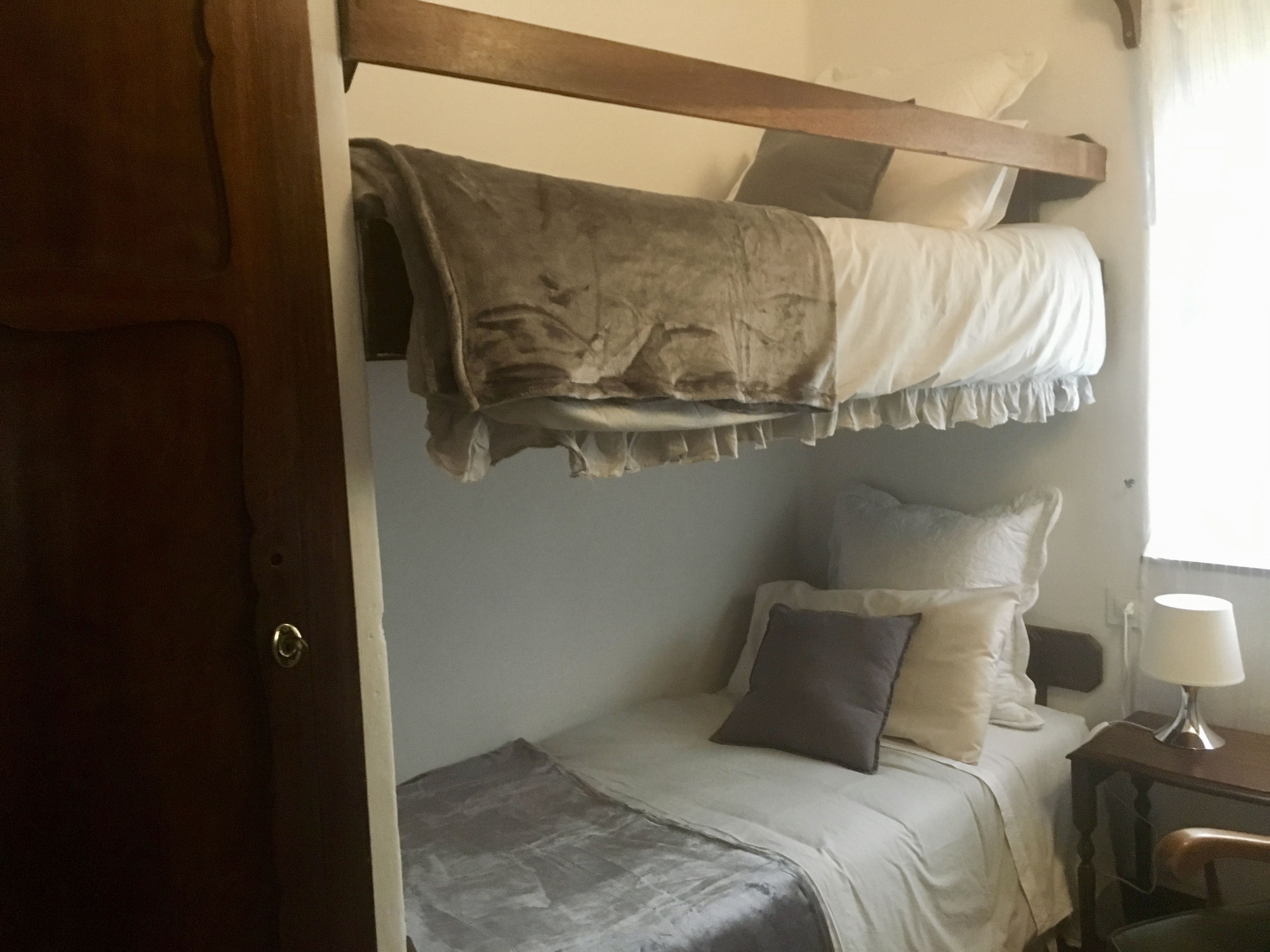 Un dormitorio con literas, una mesita de noche con lámpara y una silla.
