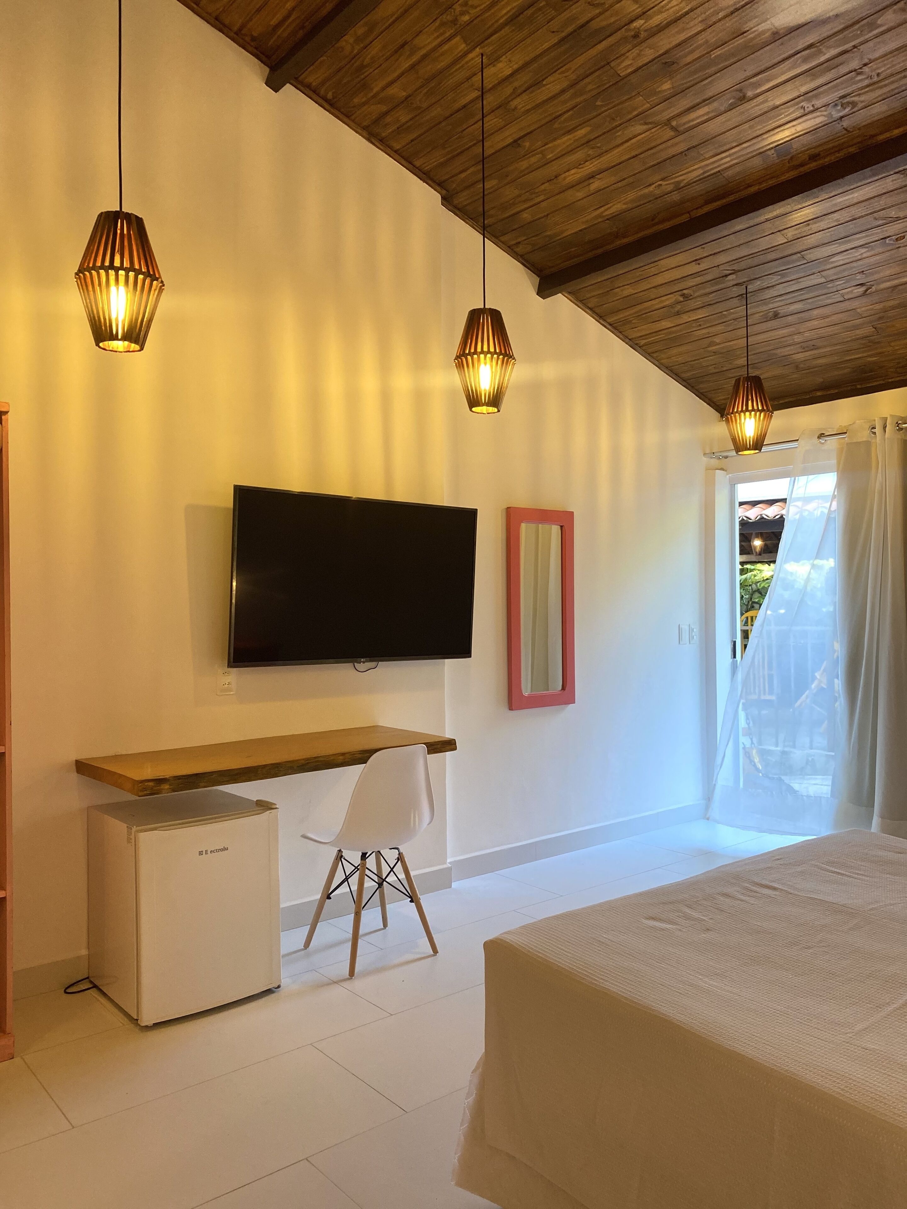 Une chambre à coucher comprenant un lit, un téléviseur fixé au mur, un petit bureau avec une chaise et un réfrigérateur.