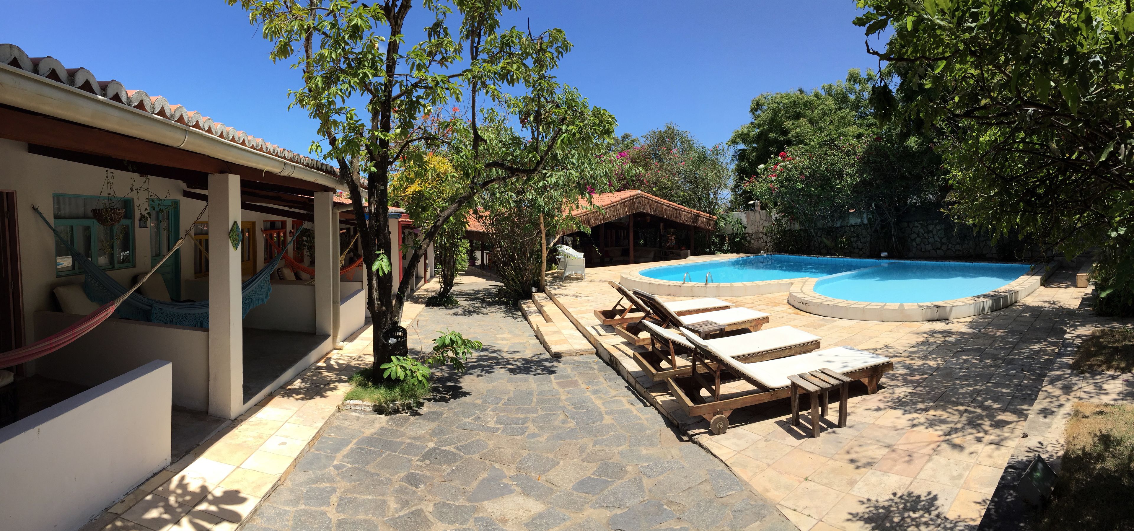 A pool area with lounge chairs, a hammock, and a small building with a thatched roof.