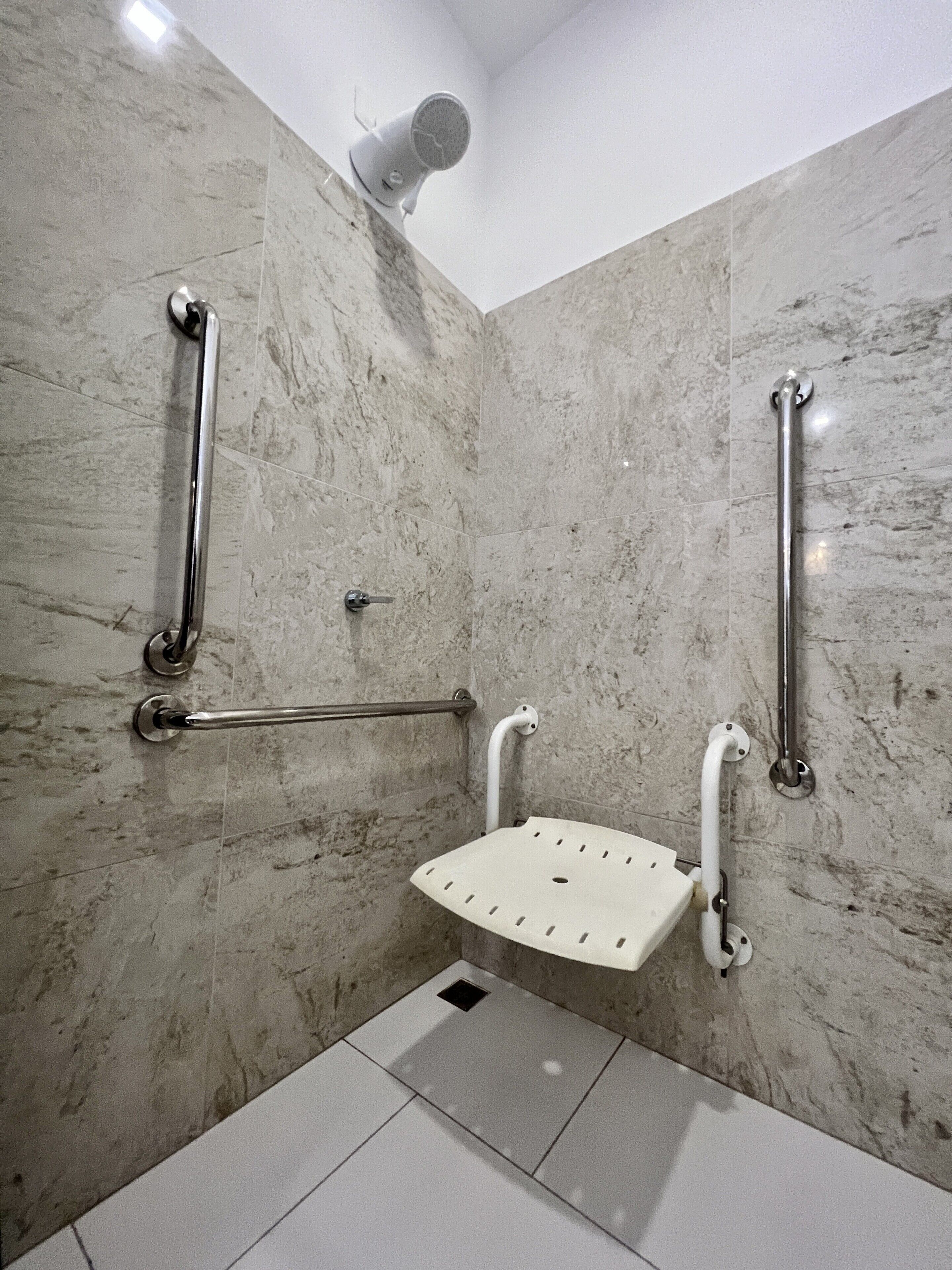 A bathroom with marble walls, a shower with a handheld showerhead, and grab bars.