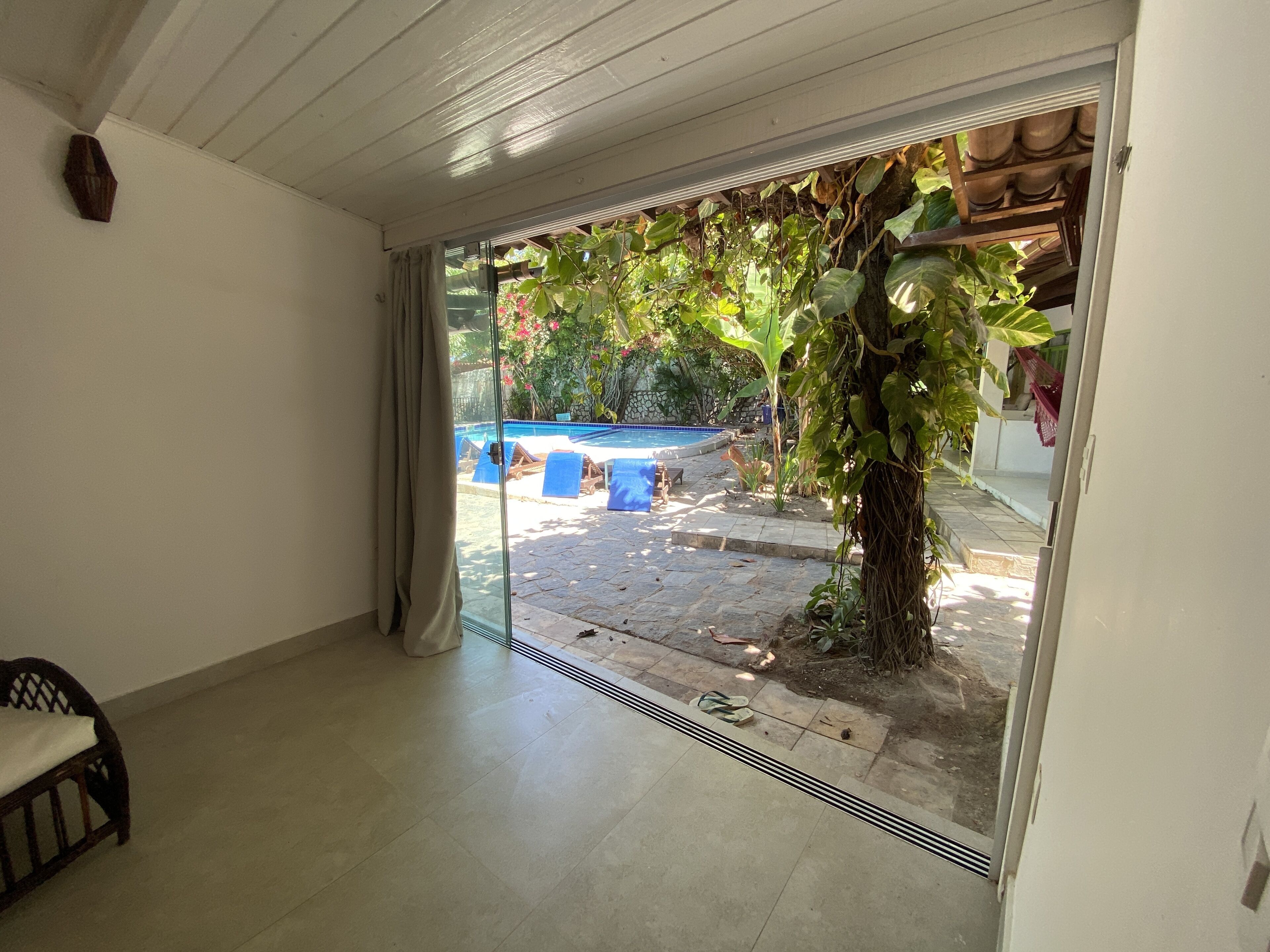 Habitación con puerta de cristal corredera que da a un jardín con piscina, mobiliario exterior y follaje.