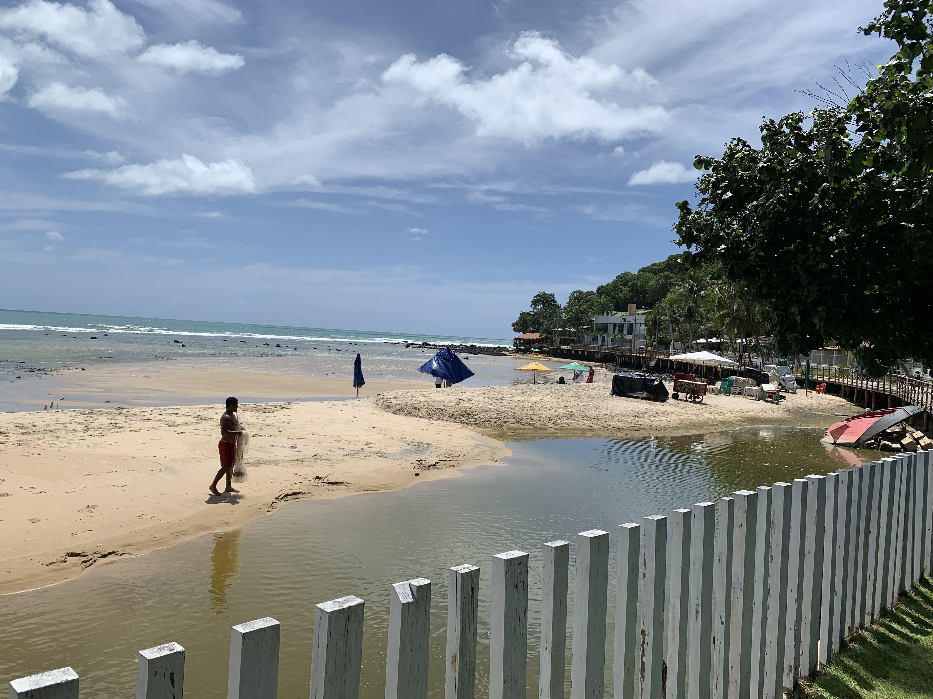 Une plage avec une clôture en bois, des parasols et un bâtiment en arrière-plan.