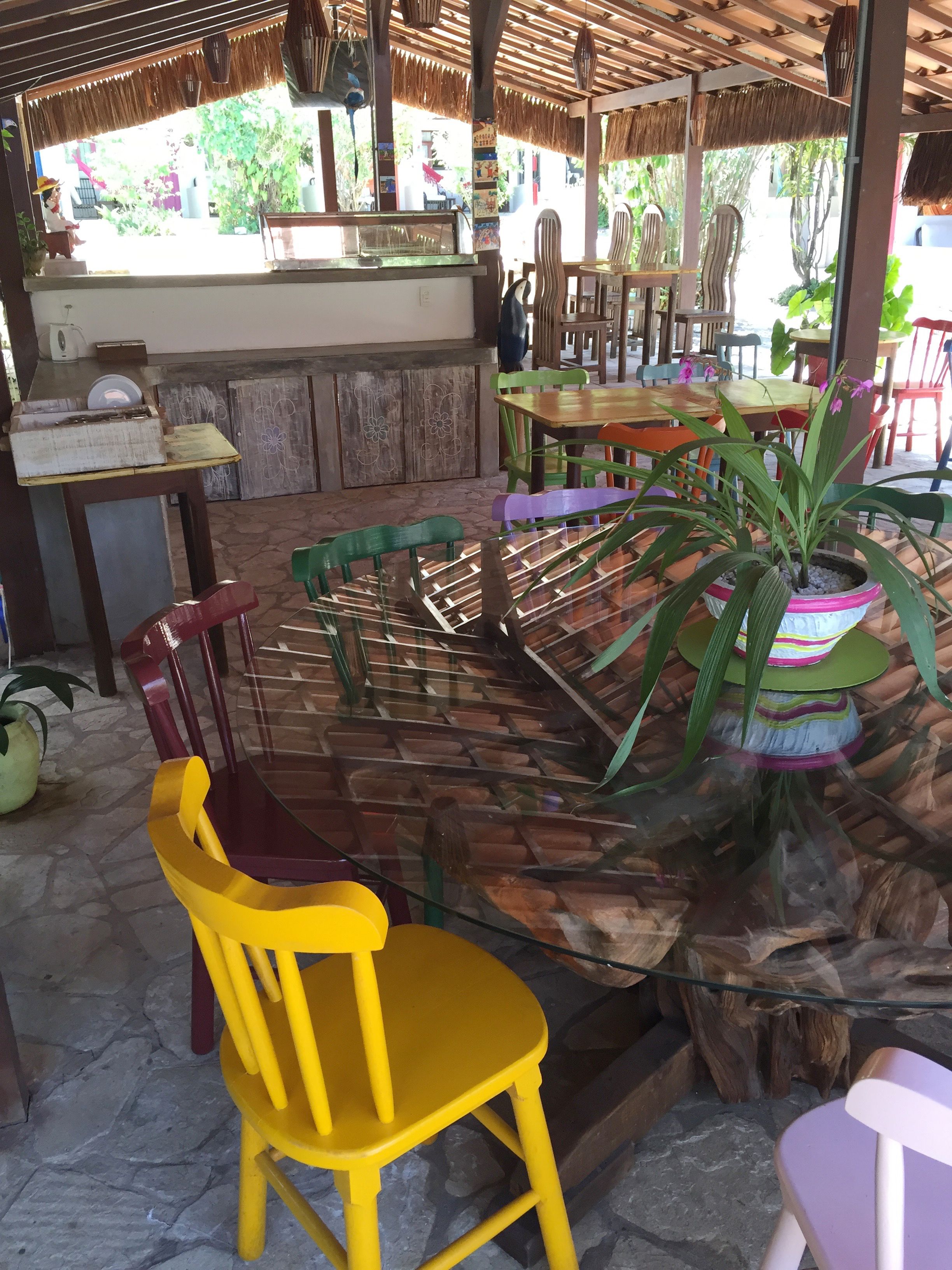 A restaurant with a thatched roof, wooden tables and chairs, and a central seating area with a glass-top table.