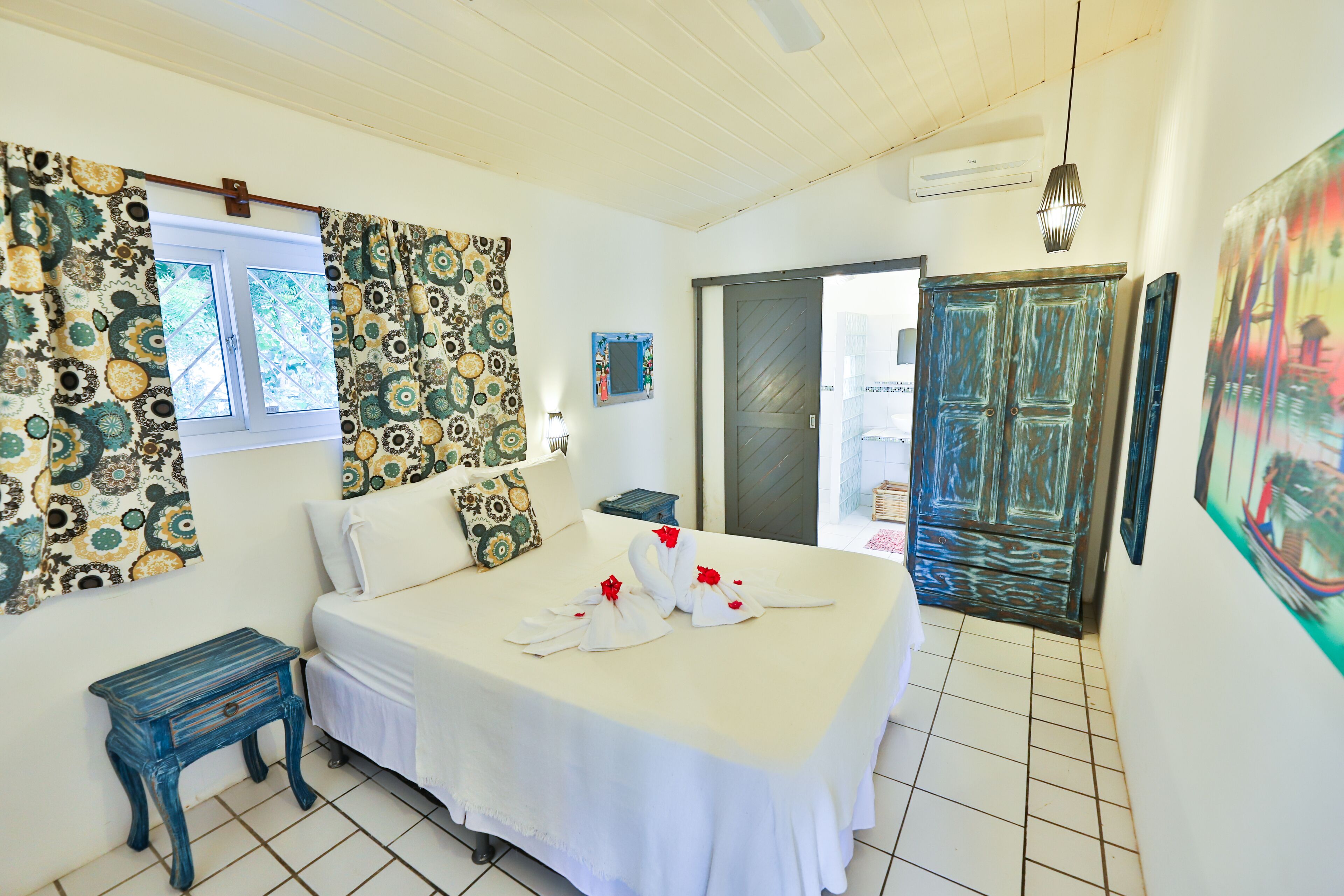 A bedroom with a bed, curtains, a nightstand, a painting, and a door leading to another room.