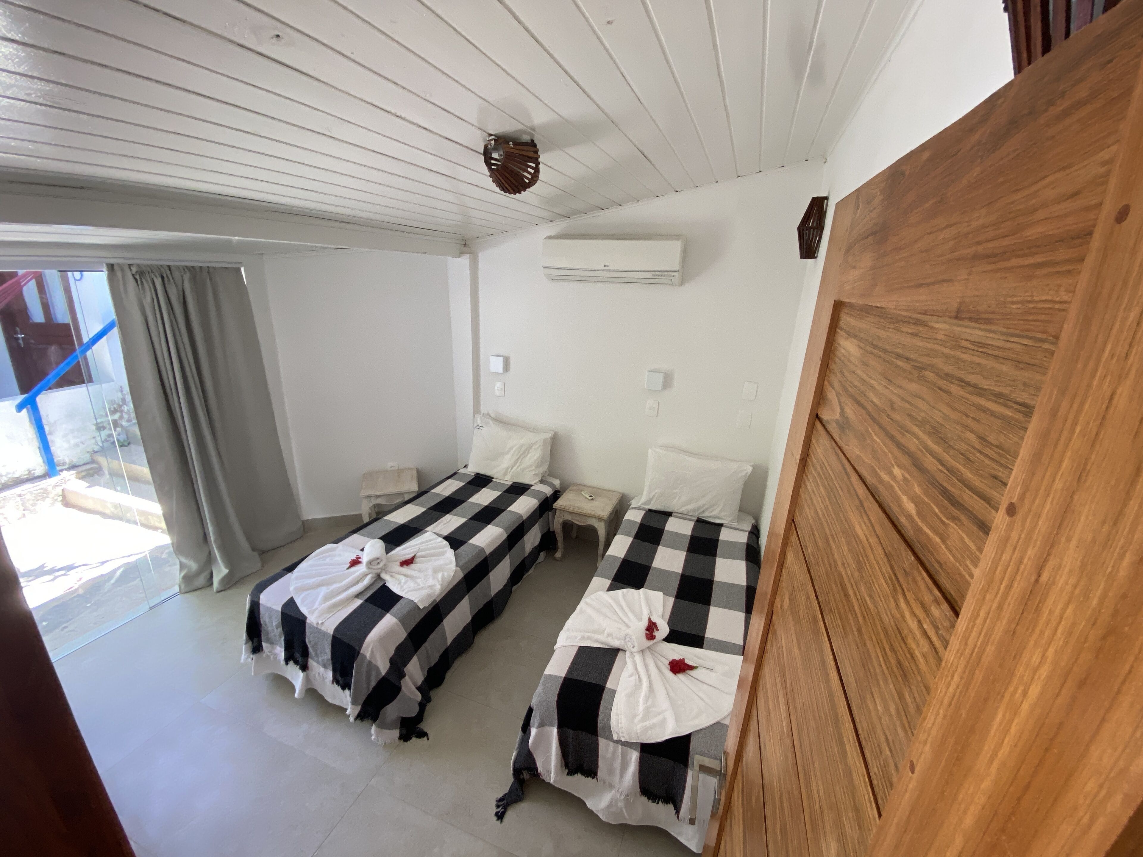 Une chambre d’hôtel avec deux lits, une tête de lit en bois, un appareil de climatisation et une vue sur l’extérieur.