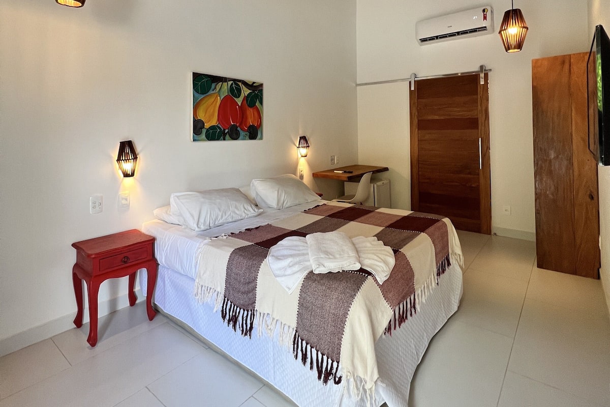 Un dormitorio con cama, mesitas de noche, ventilador de techo, luces fijadas en la pared y un cuadro colgado.