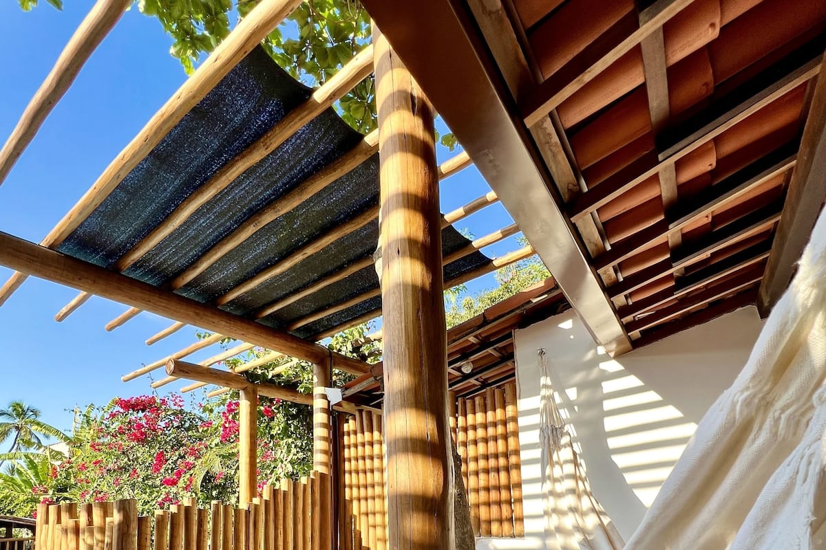 Una terraza de madera con una hamaca, una piscina y un banco de madera.
