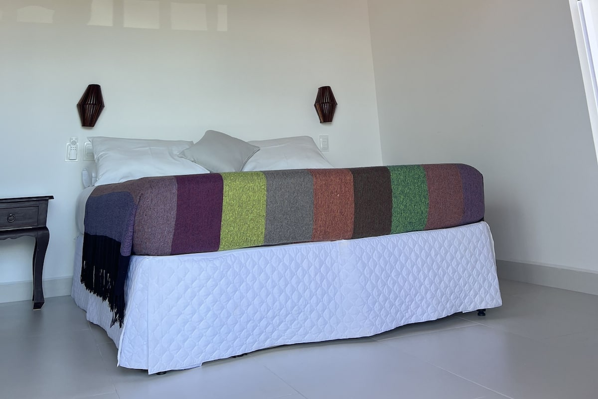 Un dormitorio con cama, vigas de madera en el techo, un equipo de aire acondicionado y una lámpara de pared.