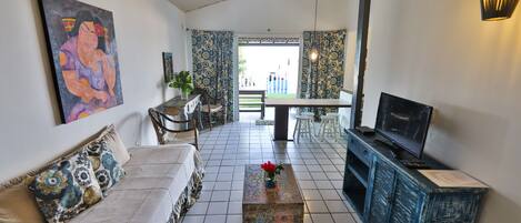 Uma sala de estar com sofá, mesa de centro, televisão e uma área de jantar com cadeiras e mesa.
