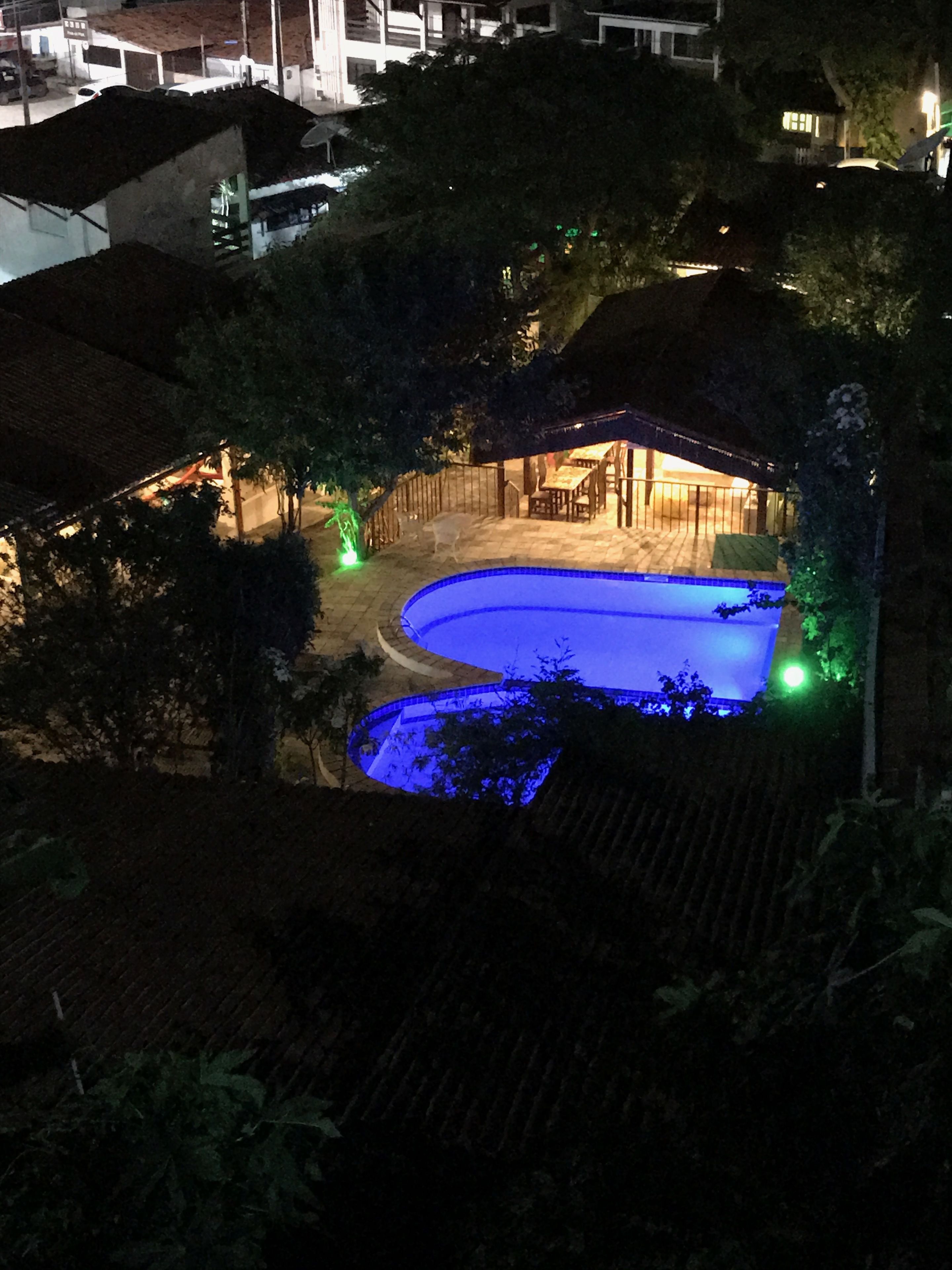 A nighttime view of a swimming pool area with a covered patio and surrounding vegetation.