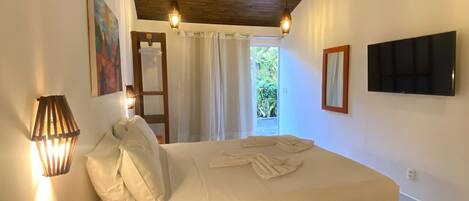 Un dormitorio con techo de madera, ventilador de techo, cama con ropa blanca, televisor montado en la pared y ventana con cortinas.