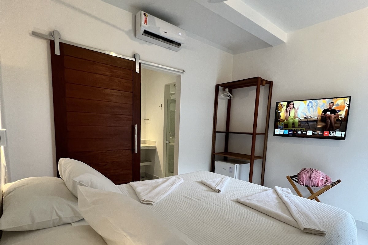 Una habitación de hotel con cama, televisor, aire acondicionado y ventilador de techo.