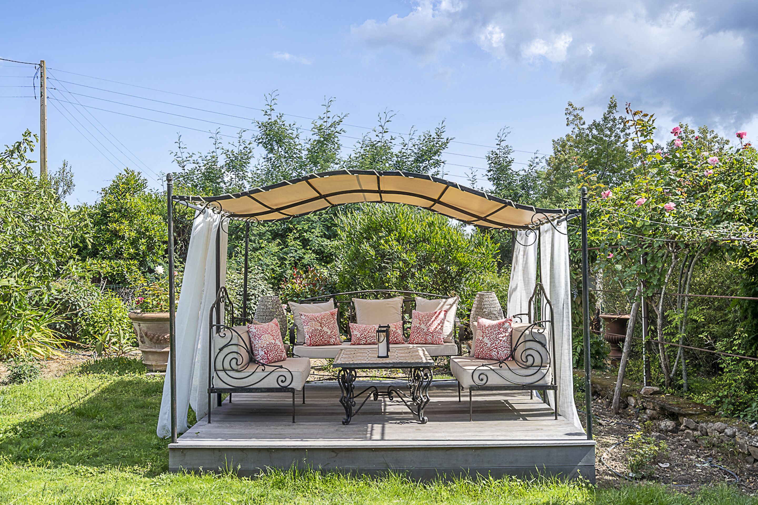 Une terrasse de jardin avec un coin salon agrémenté de coussins, une table et un auvent.