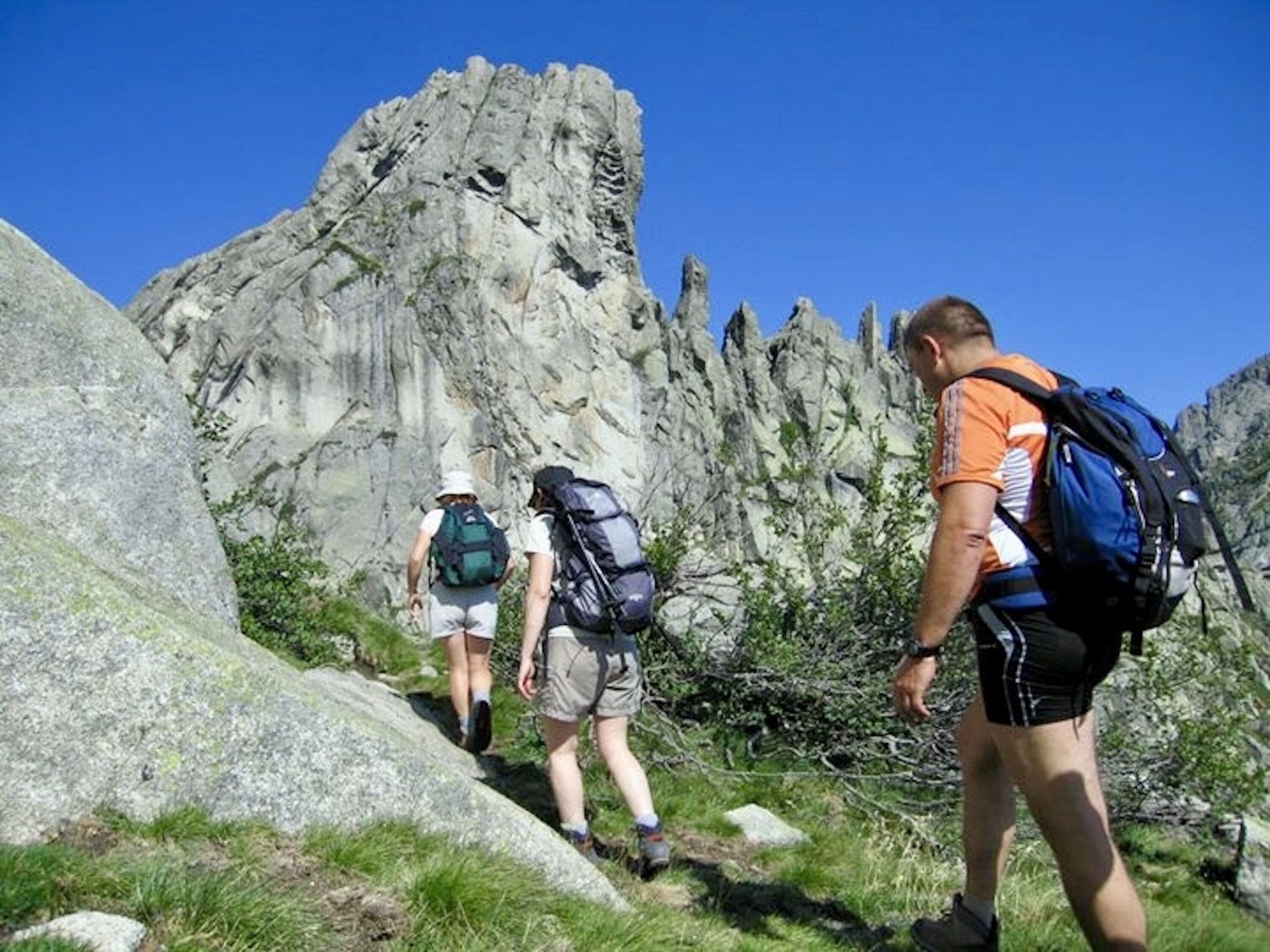 Un grupo de excursionistas en un sendero rocoso con grandes piedras y vegetación escasa.