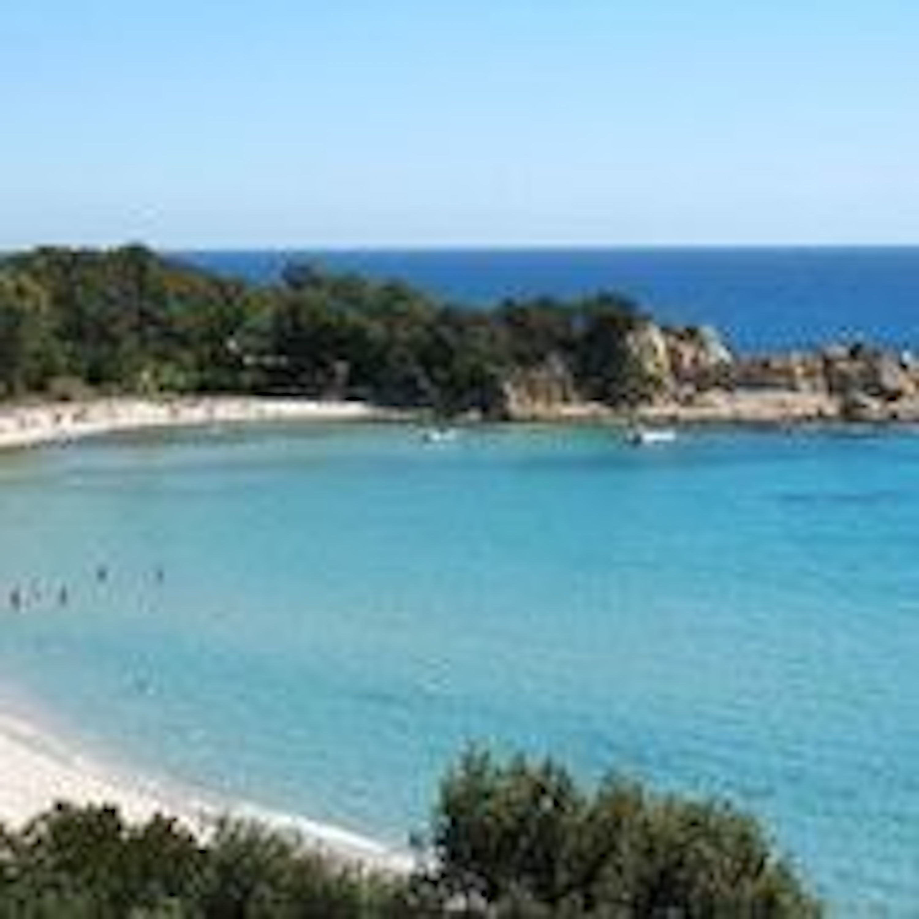 Una zona costera con aguas azul cristalino, una playa de arena y abundante vegetación.