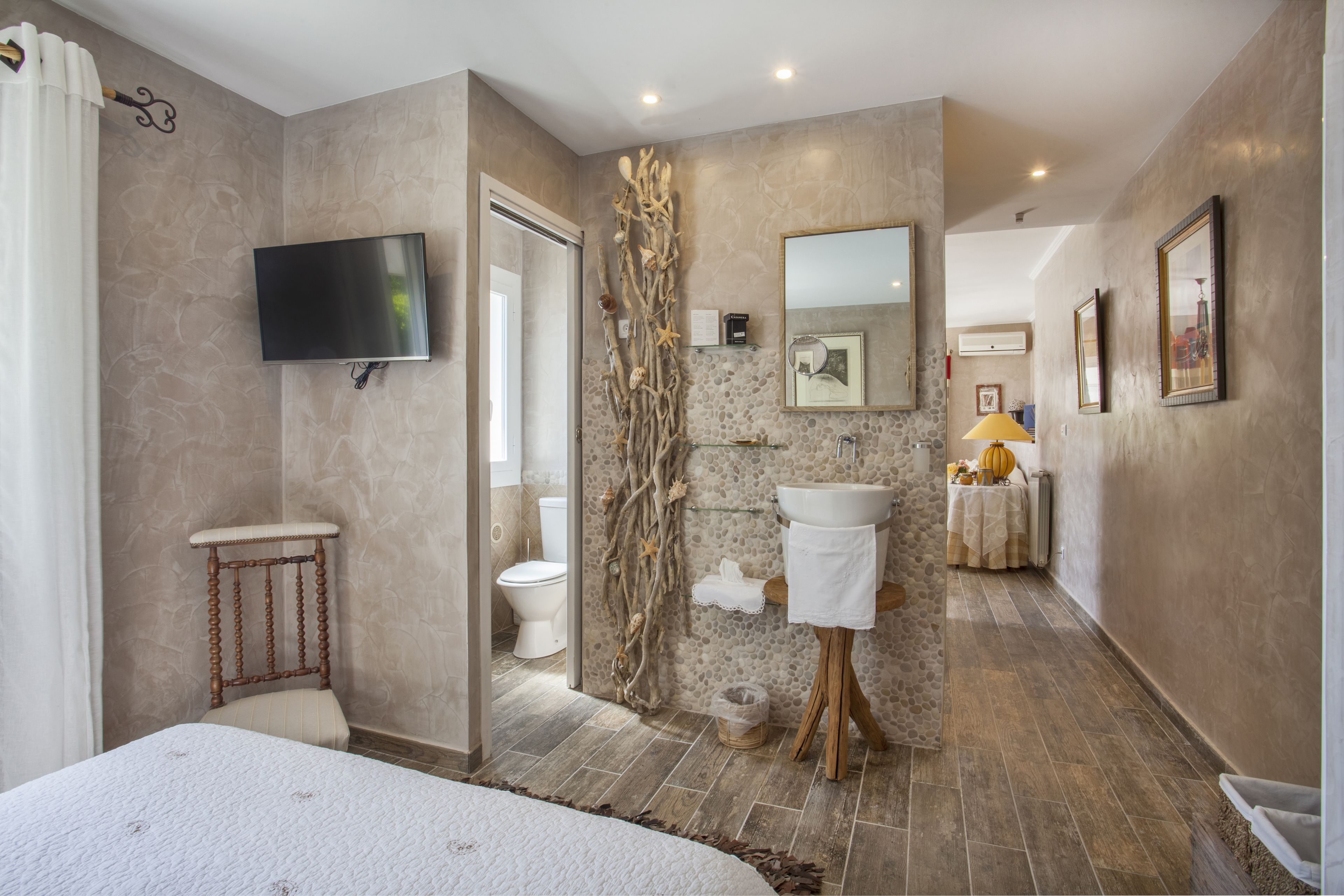 Un baño con pared de piedra, televisor montado, lavamanos y espejo.