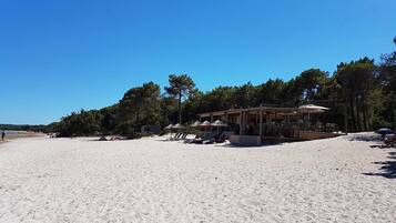 A beach with a wooden structure providing shade, surrounded by trees.