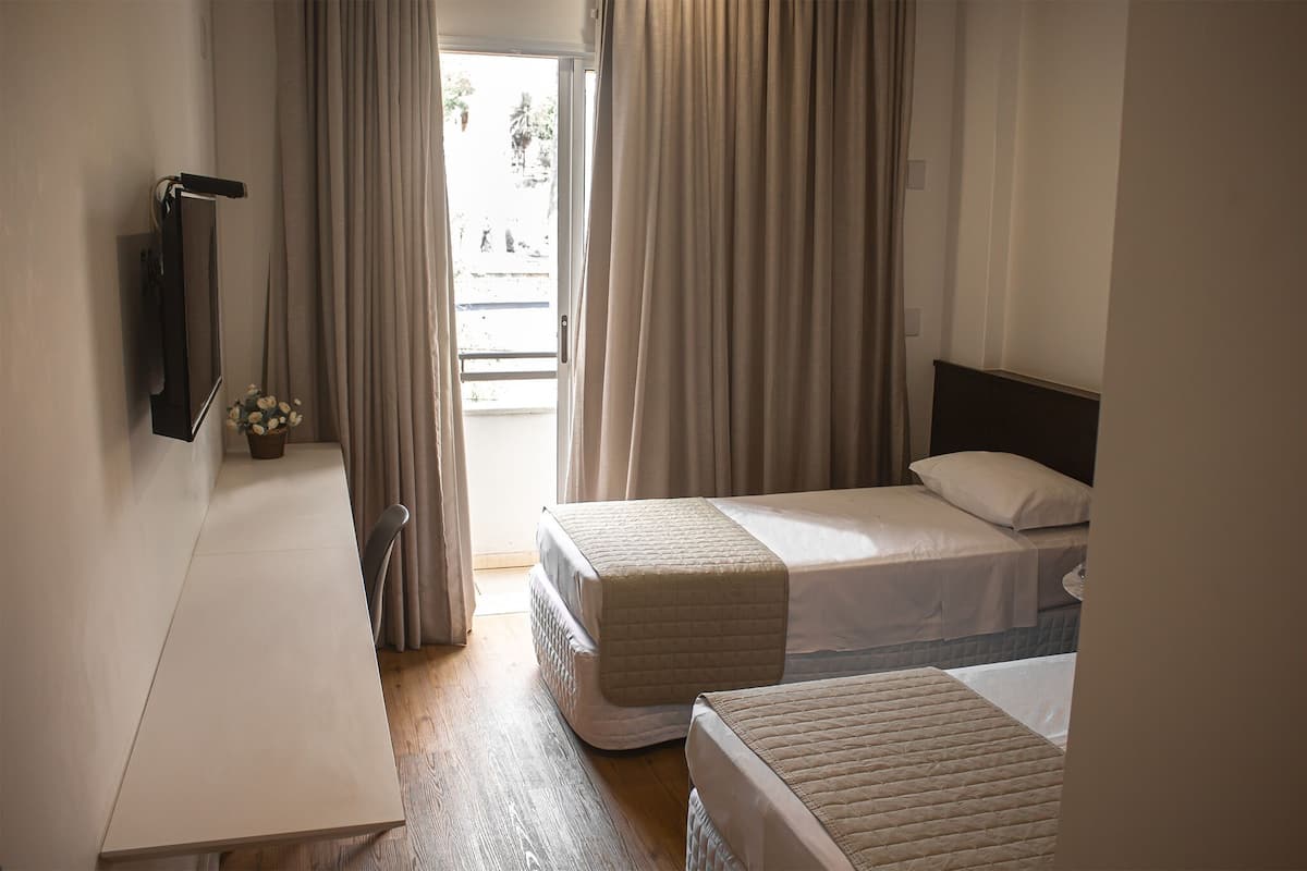 A hotel room with two beds, a desk, and a view of the outdoors.