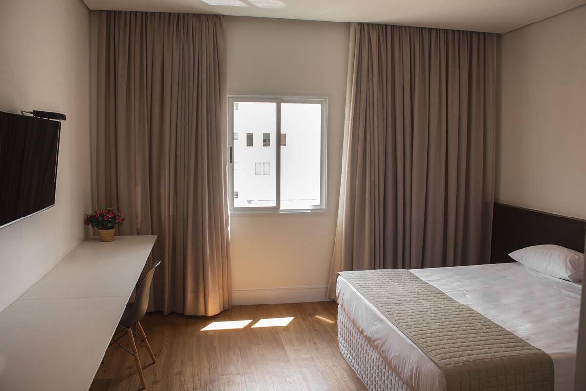 A hotel room with a bed, a desk, and a window with curtains.