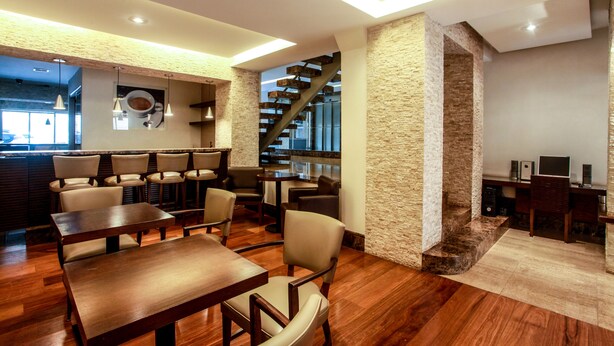 Un restaurante moderno con mesas y sillas de madera, un muro de acento de piedra y una escalera que sube a un nivel superior.