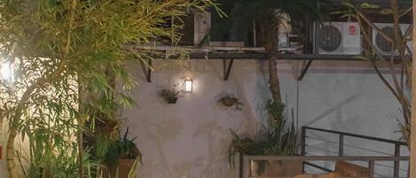 An outdoor area with potted plants, a wooden bench, and a staircase leading to an upper level.