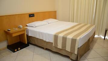A hotel room with a bed, a nightstand, a control panel, and a curtain.