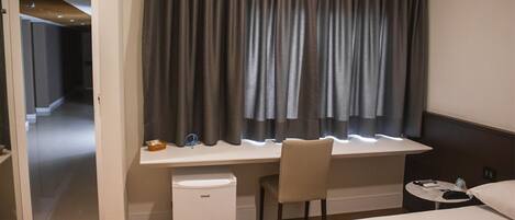 Habitación de hotel con cama, escritorio con silla, una mesita con control remoto y un refrigerador pequeño.