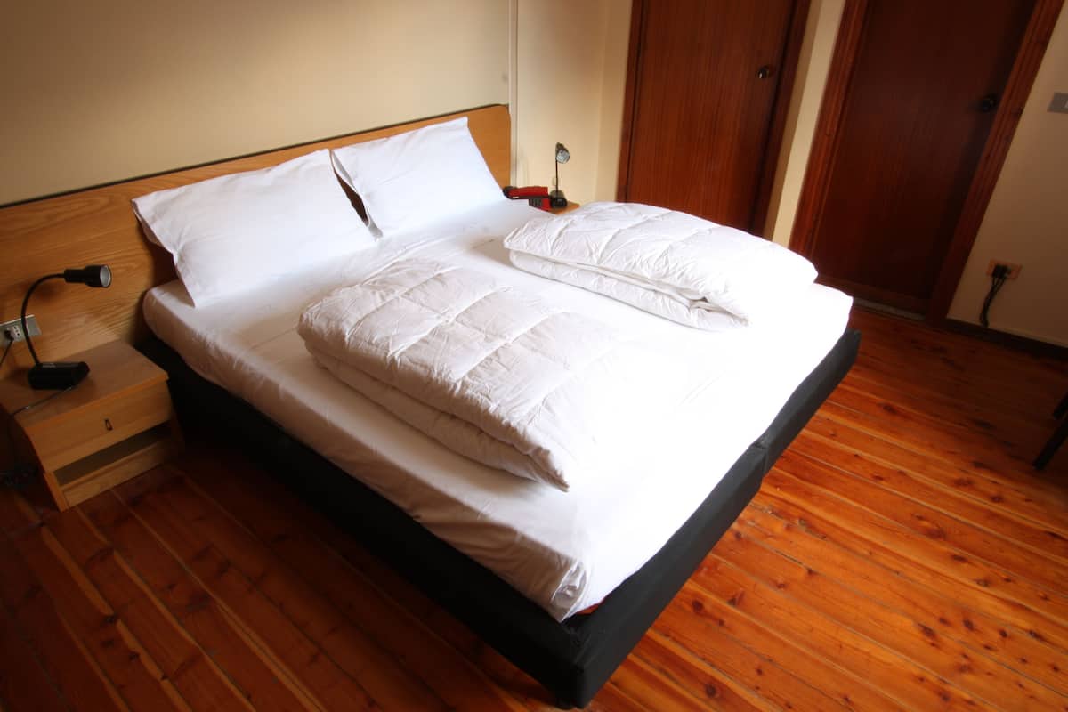 A neatly made bed with white linens in a room with wooden flooring and a wooden headboard.