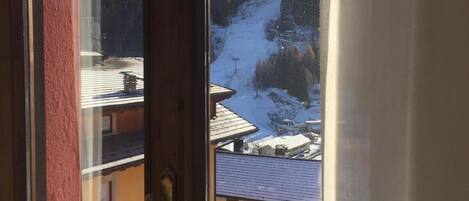 A window view of a mountain landscape with a ski slope and buildings below.