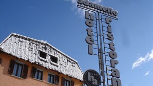 Un letrero de hotel con el nombre 'Adamello Hotel' y un emblema circular con la letra 'ha' en el centro.