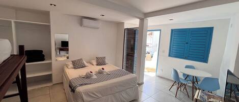 Un dormitorio con cama, escritorio, silla, televisión y baño visible a través de una puerta.