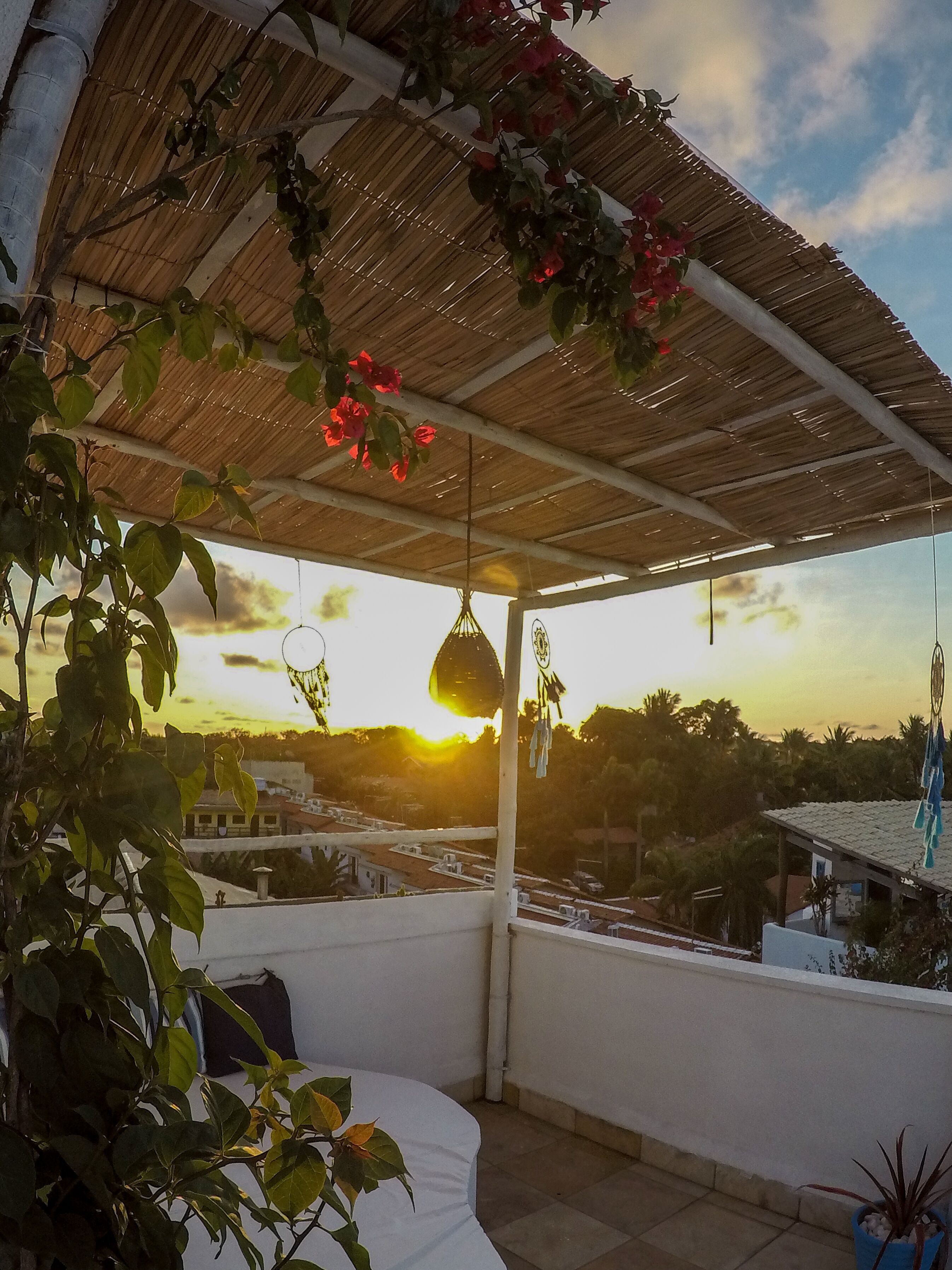 Ein überdachter Balkon mit Blick auf den Sonnenuntergang, ein hängender Traumfänger und Topfpflanzen.