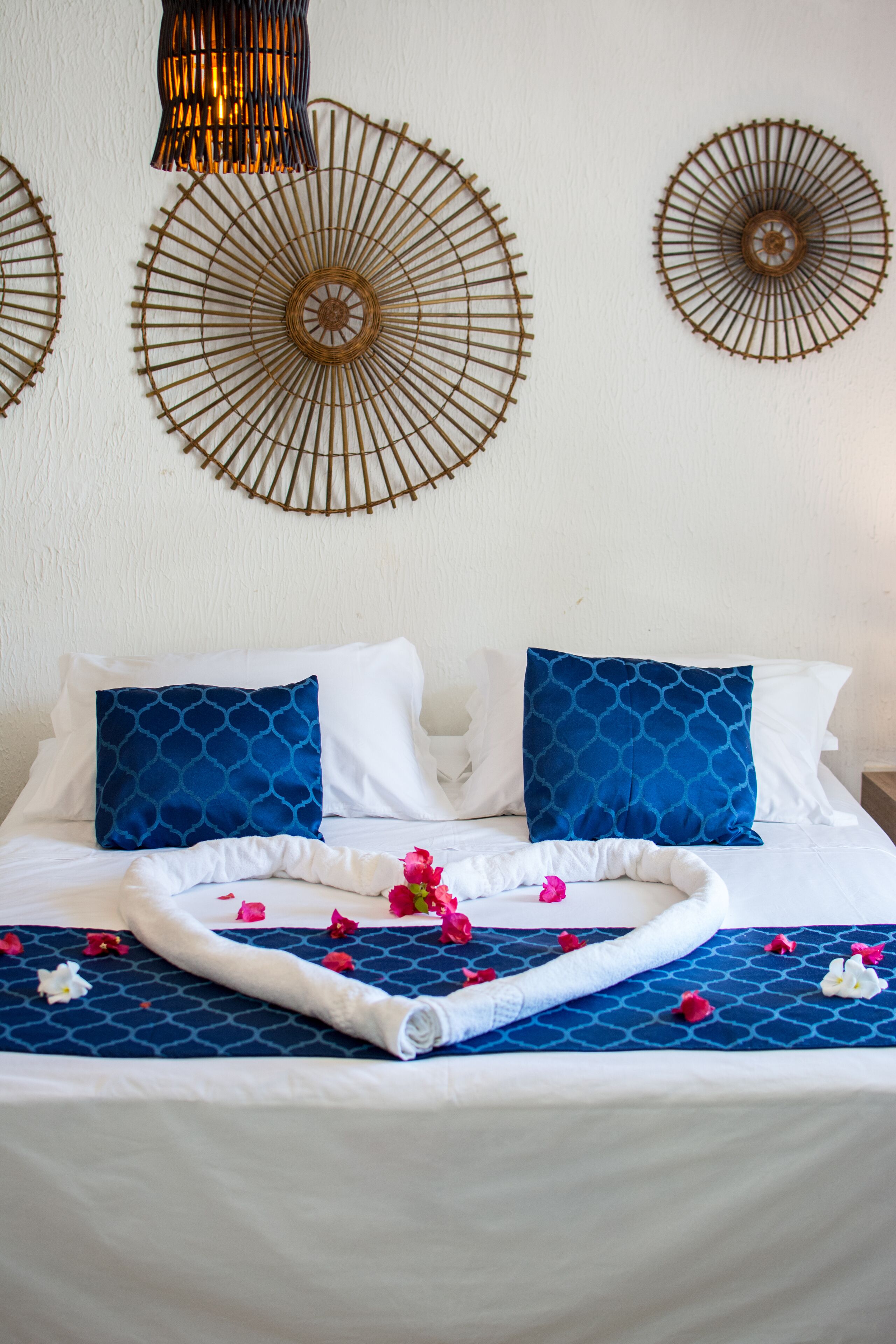 Una cama bien hecha con almohadas estampadas en azul, una colcha blanca y un adorno decorativo en la pared.