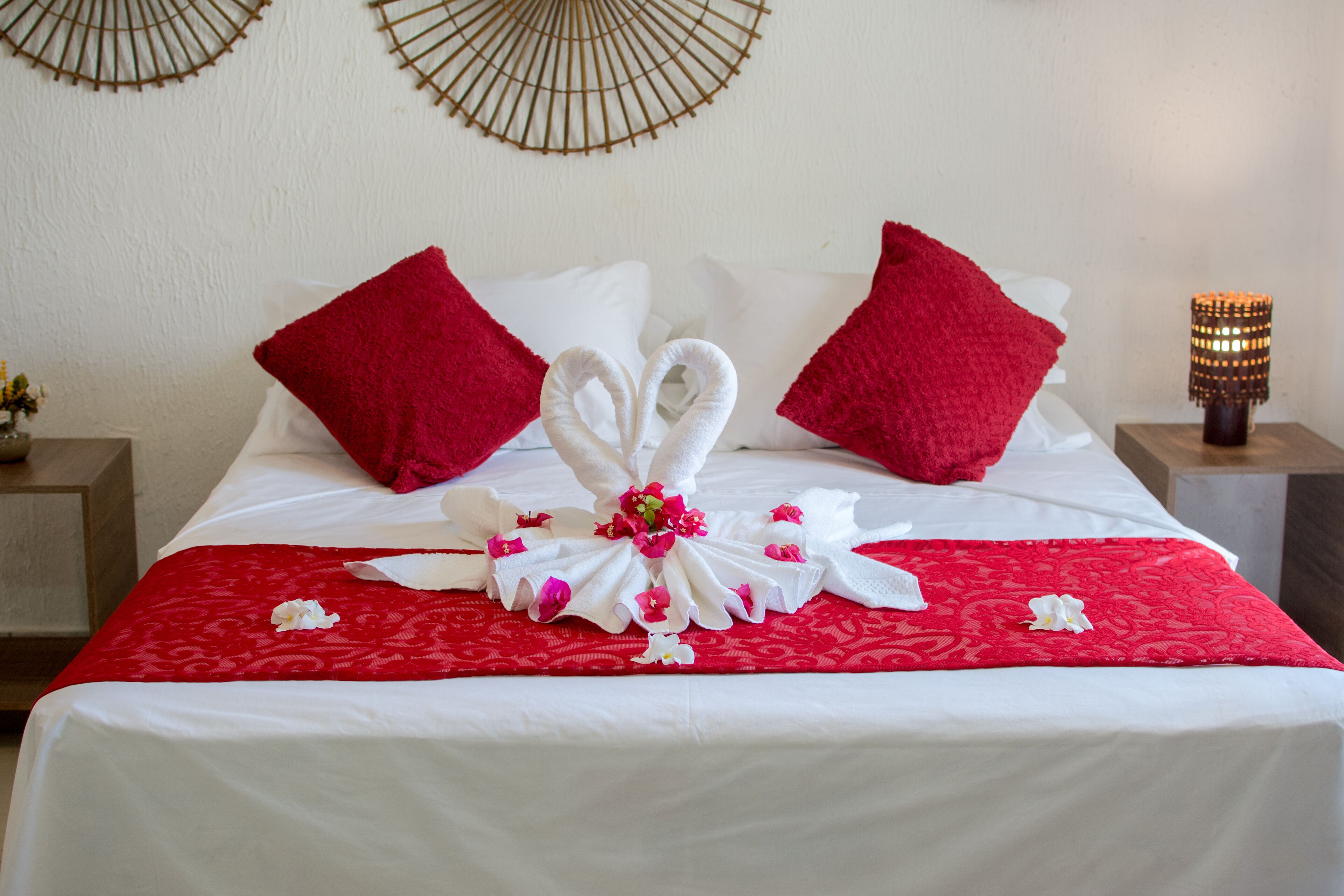 A neatly made bed with a red and white bedspread, two red pillows, and a decorative towel arrangement on the bed.