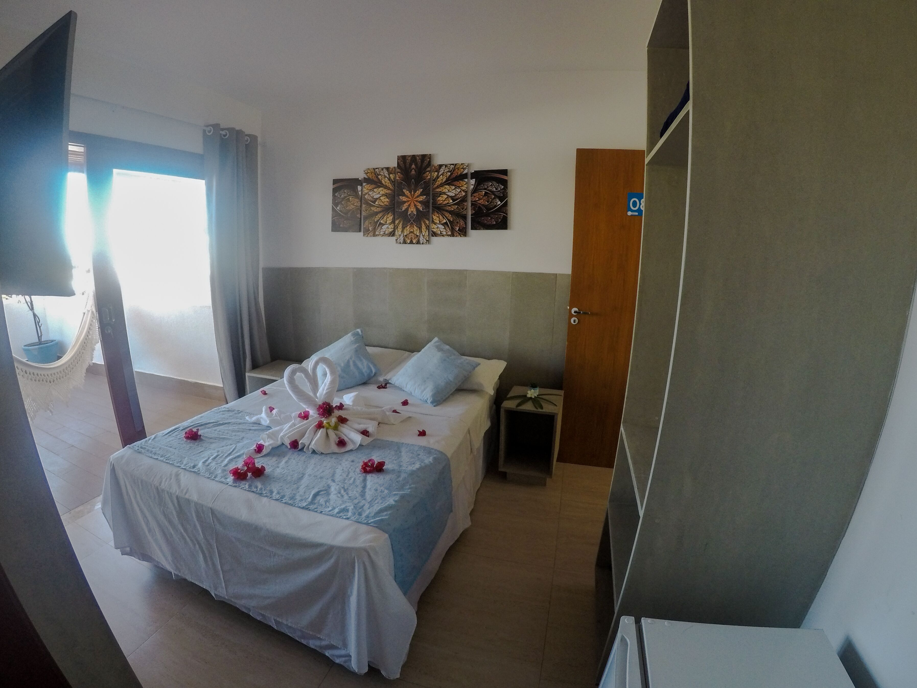A hotel room with a bed, a nightstand, a wall art piece, and a door.