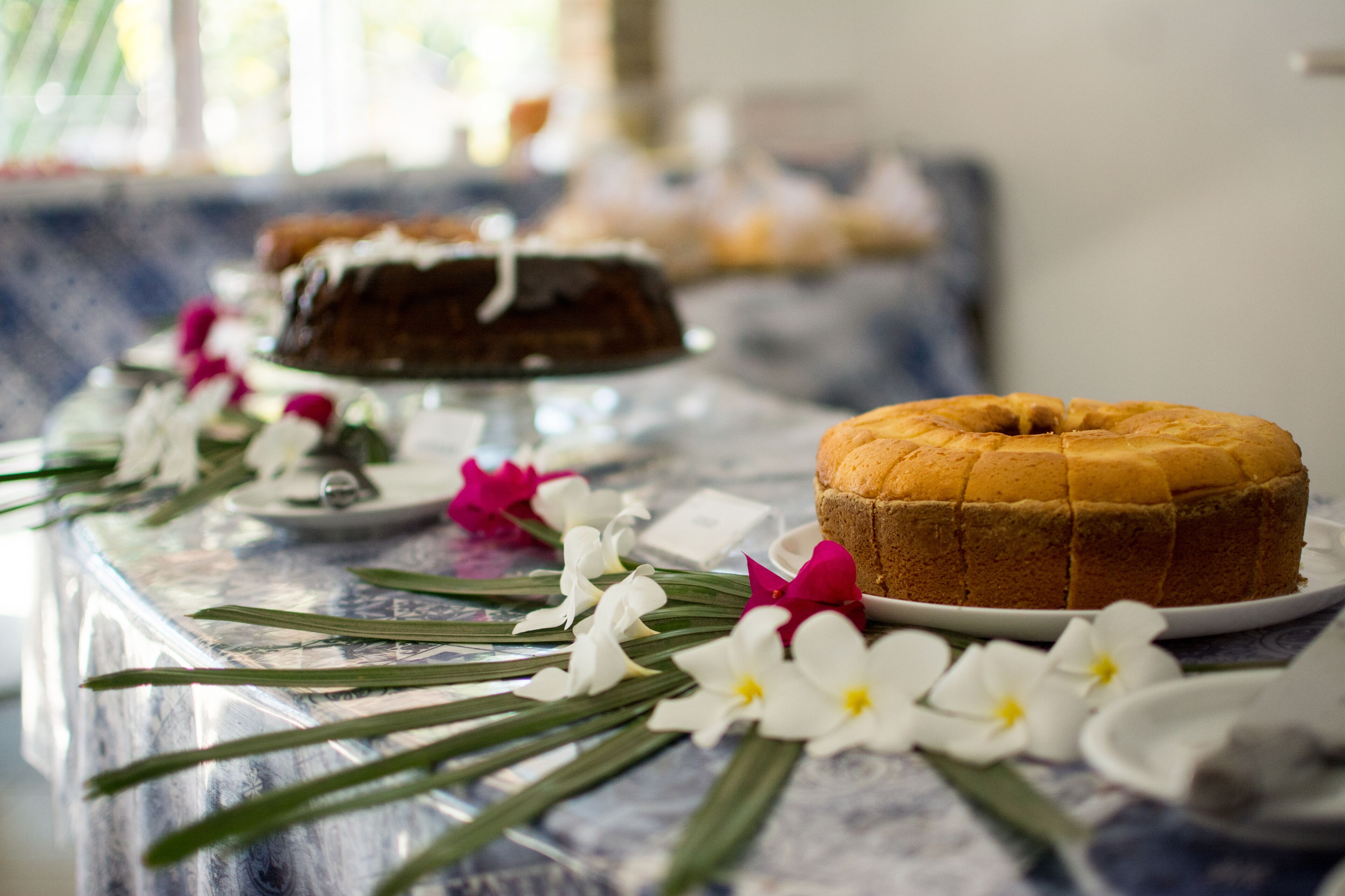 Una mesa con un pastel Bundt y un pastel redondo sobre platos blancos, rodeada de flores blancas y rosas.