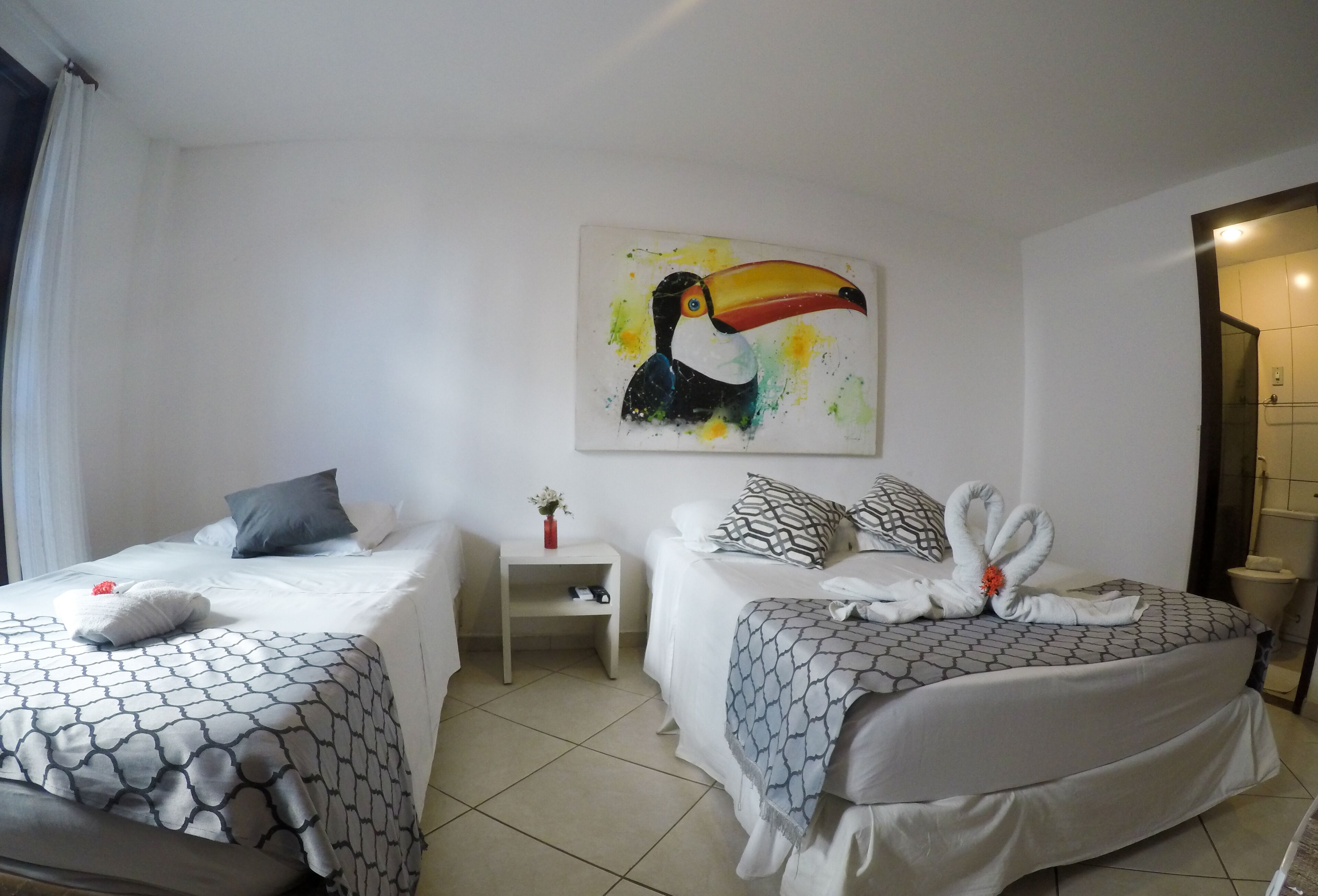 Ein Hotelzimmer mit zwei Betten, einem Papageienporträt und einem kleinen Tisch mit einer Vase.