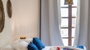 Et hotelværelse med seng, et stort badekar med rosenblade, et vindue med gardiner og vægdekorationer.