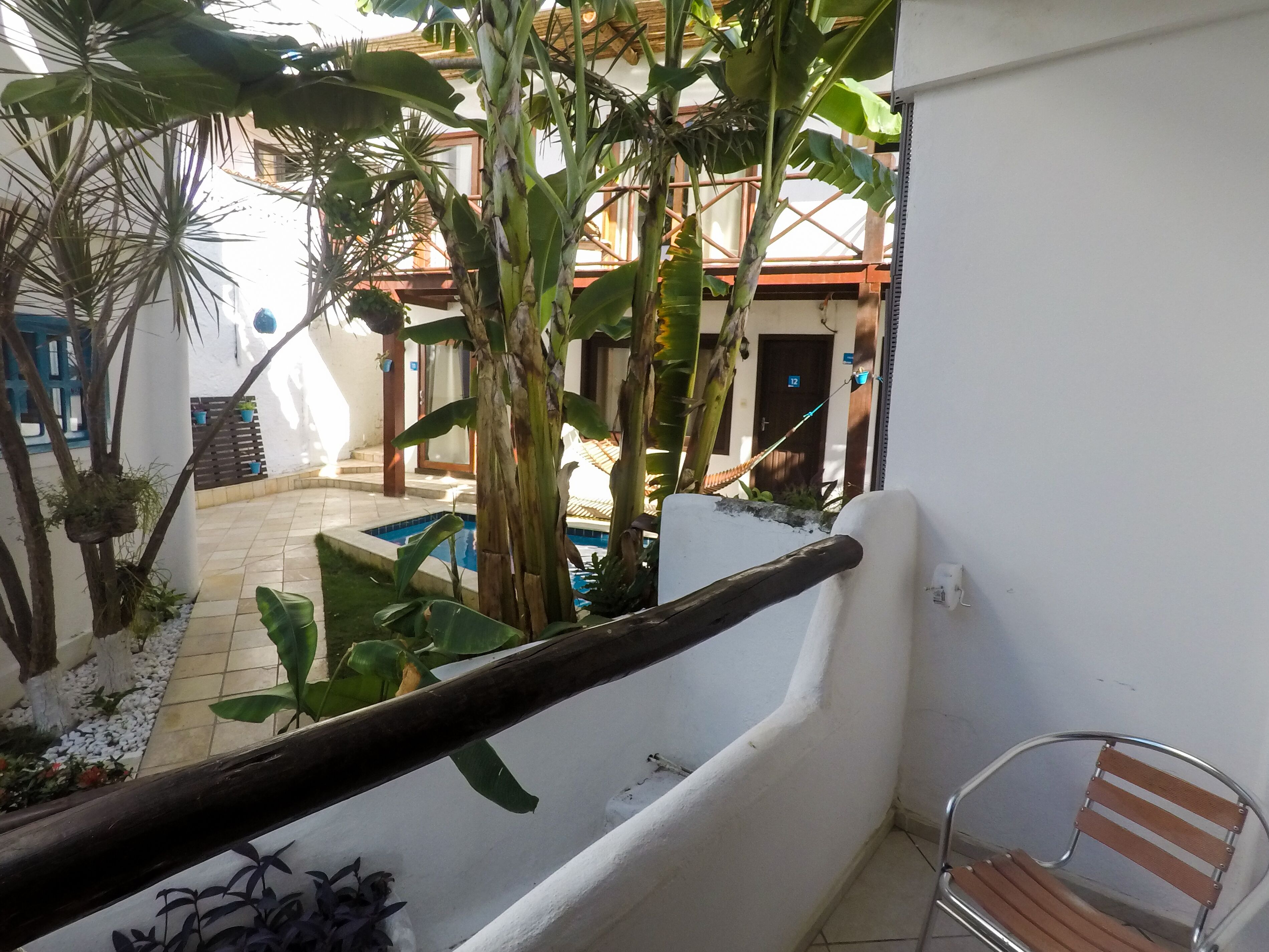 Un balcón con vistas a una piscina, rodeado de abundante vegetación y una pared blanca.