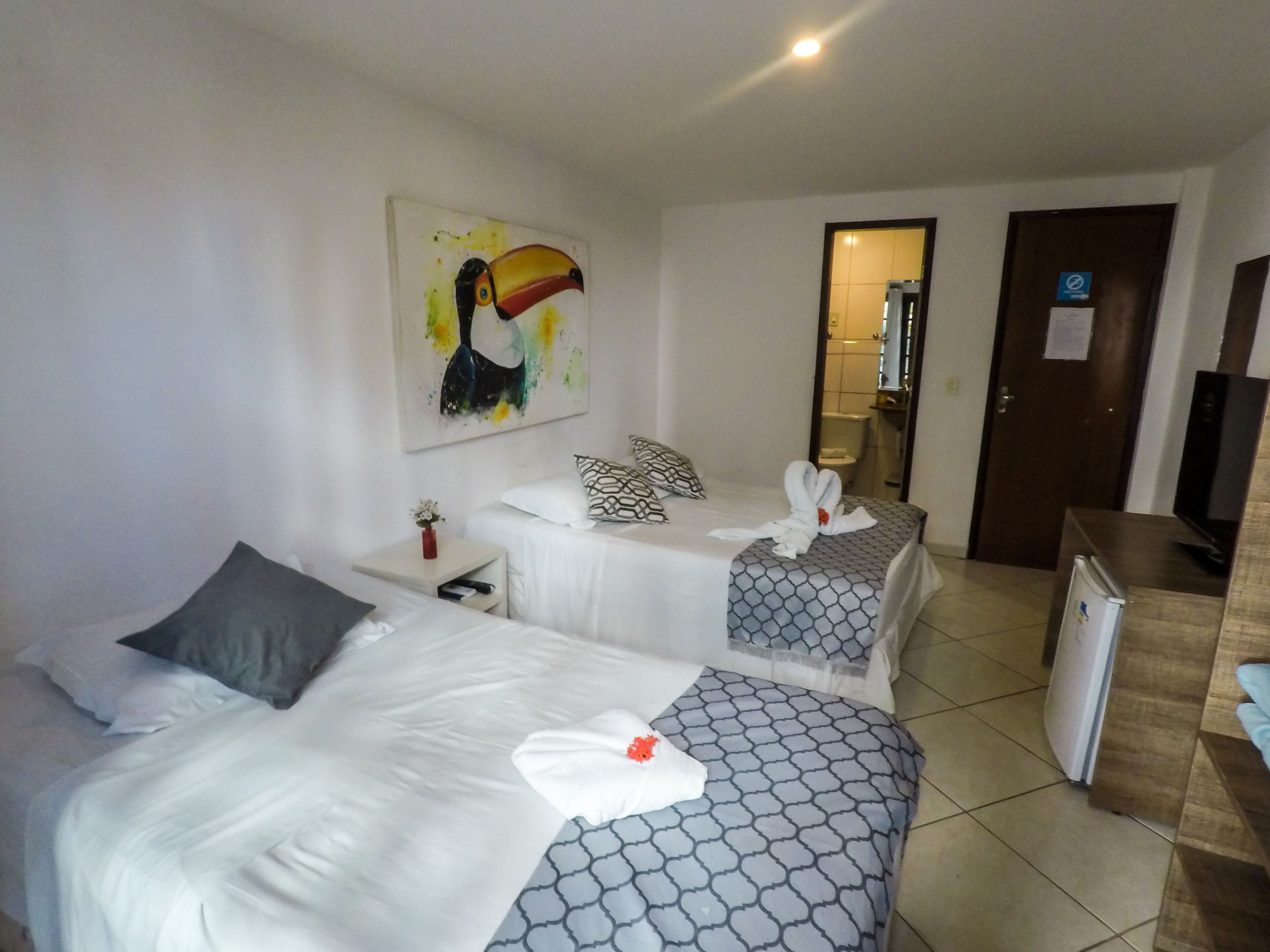 Une chambre d’hôtel avec deux lits, un tableau au mur, une petite table avec un vase et une télévision.
