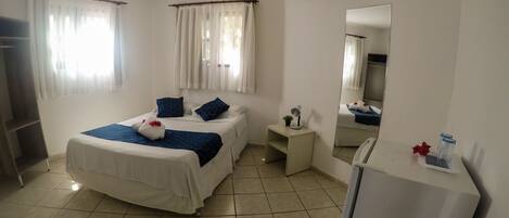A hotel room with a bed, a small desk, a mirror, and an air conditioner.