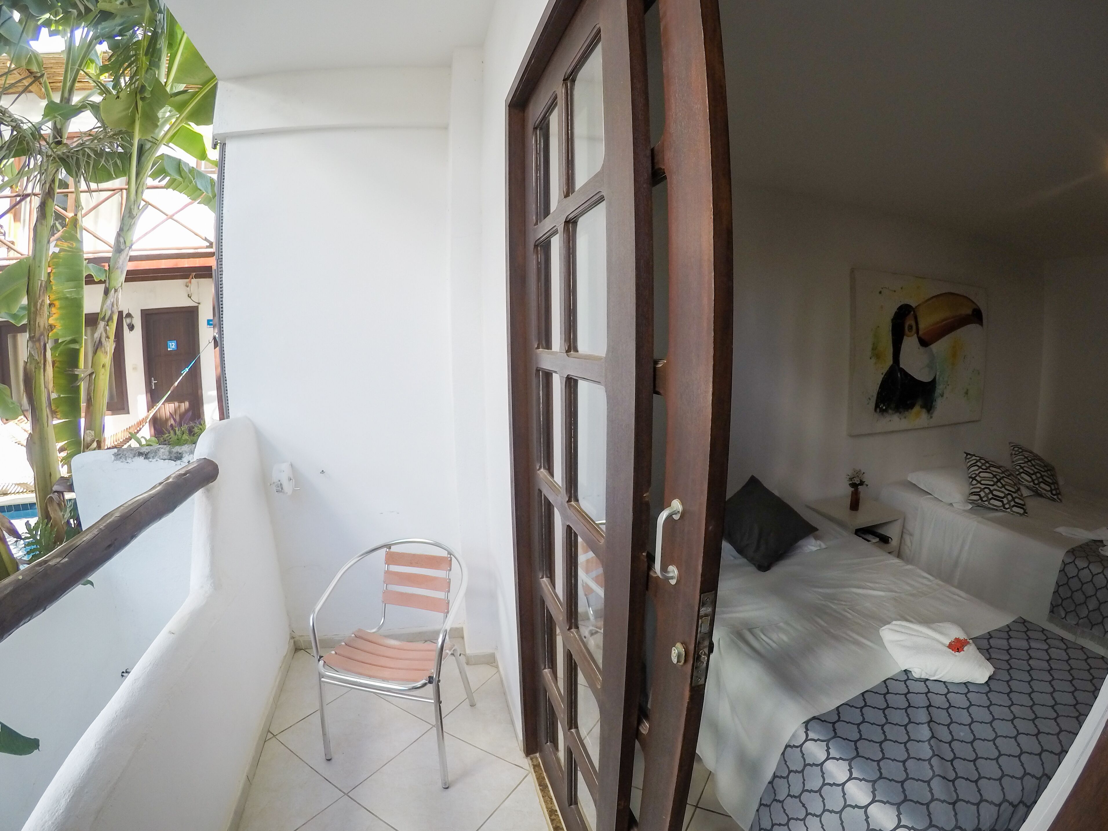 A room with a bed, a chair, and a door leading to an outdoor area with a view of a building and a tree.