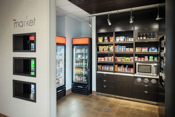 Eine Küchenzeile mit einer Mikrowelle, einem Kühlschrank und Regalen voller Snacks und Getränke.