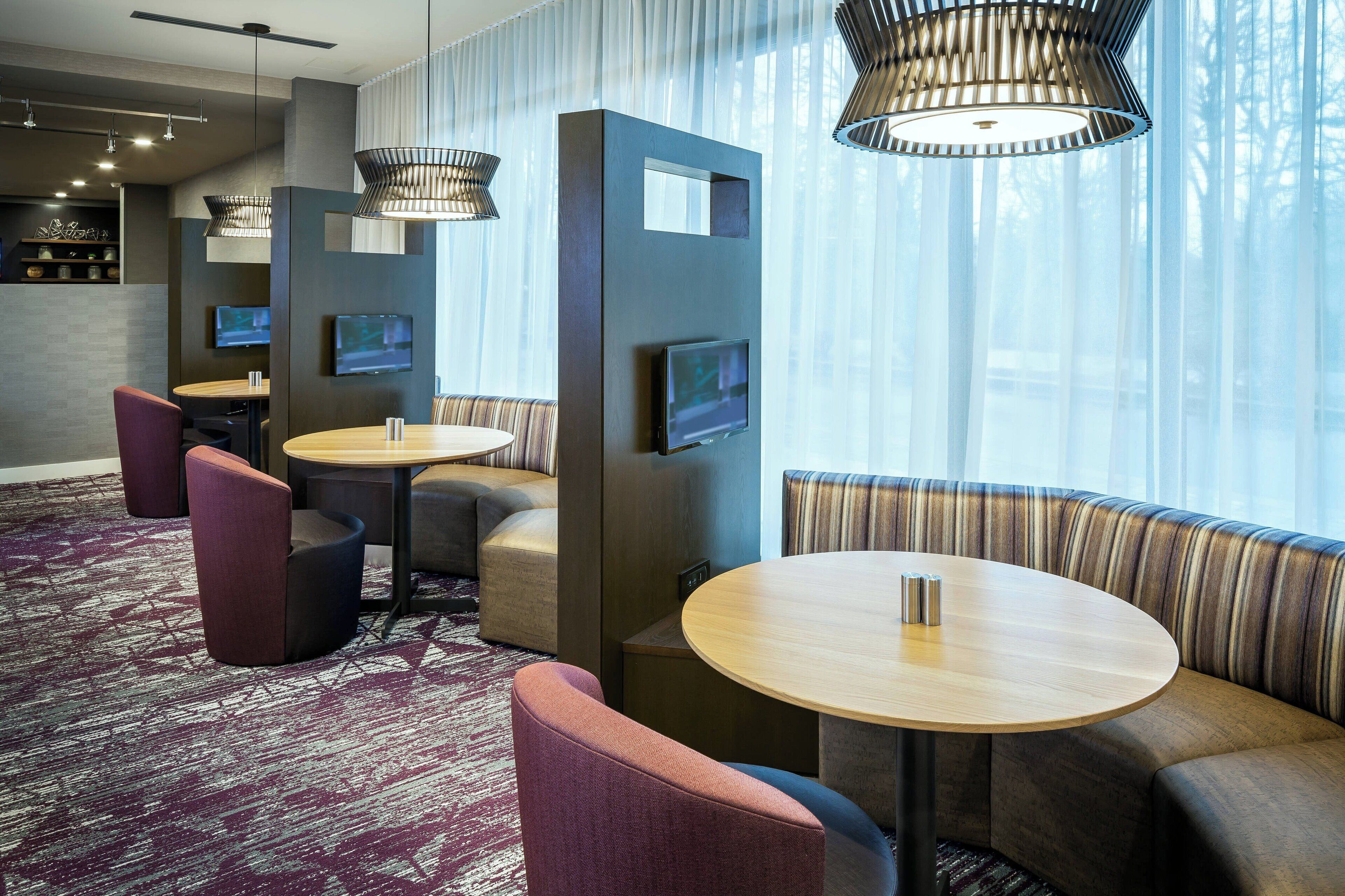 A modern hotel lobby with seating areas, a TV, and a patterned carpet.