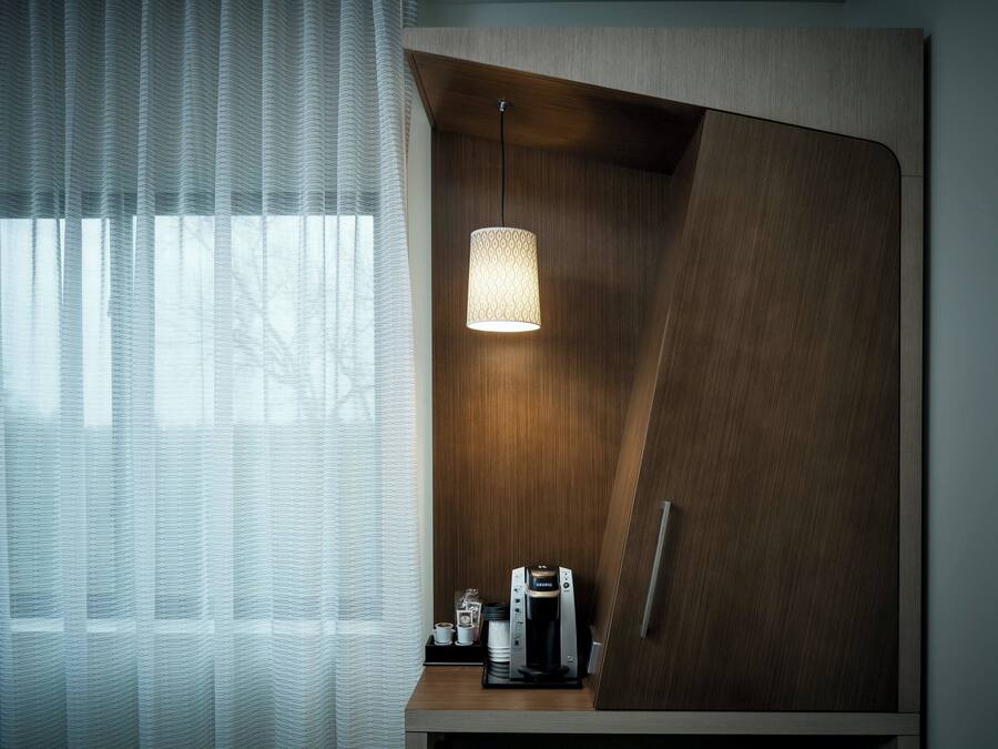 A modern room with a wooden cabinet, a coffee maker, and a hanging light fixture.